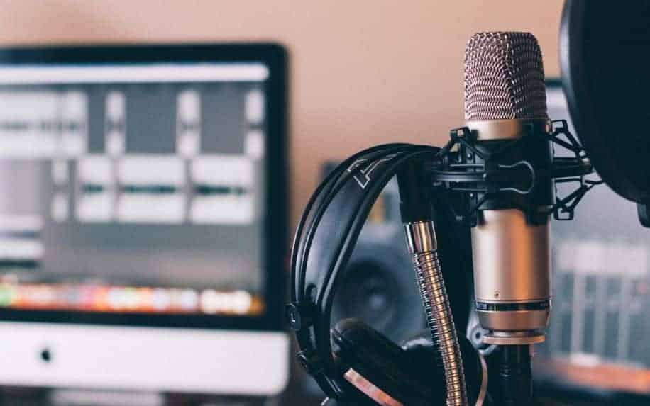 A home office Podcast setup, with headphones resting on a microphone and an iMac in the background.