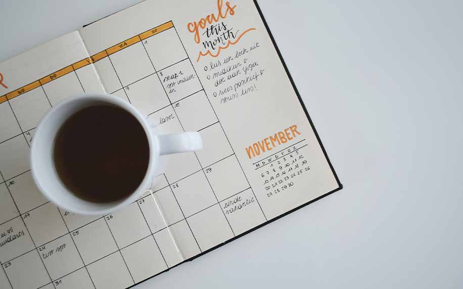 A cup of coffe sitting on a copywriters schedule on a white table