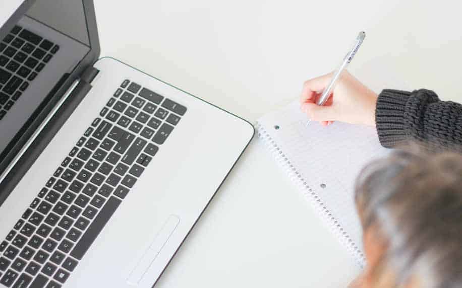 Woman writing her conclusion on paper beside her computer