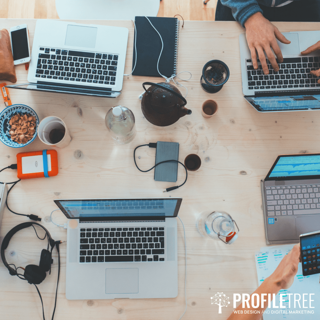 Image of several laptops together on a desk with people working on them